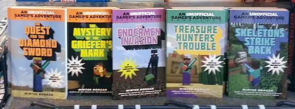 Image taken at a bookfair, depicting several unlicensed paperback Minecraft novels. Titles going left-to-right: "The Quest for the Diamond Sword", "The Mystery of the Griefer's Mark", "The Endermen Invasion", "Treasure Hunters Trouble", and "The Skeletons Strike Back". All books carry the stamp, "An UNOFFICIAL Gamer's Adventure," with the word "unofficial" given special visual emphasis.